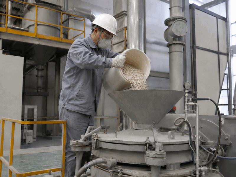 Chinese technician loading composite ceramic grinding beads into industrial milling equipment